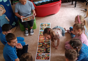 Dzieci siedzą w siadzie skrzyżnym na dywanie.