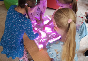 Dziewczynki rysują paluszkami na piasku.