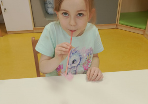 Dziewczynka dmucha przez słomkę na piórko.