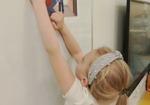Dziewczynka zawiesza obrazek na tablicy.