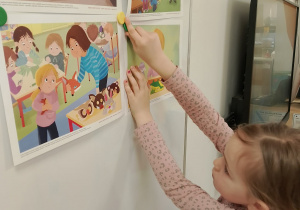 Dziewczynka zawiesza obrazek na tablicy.