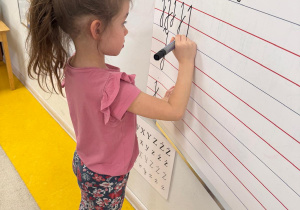 Dziewczynka pisze na tablicy literę J.