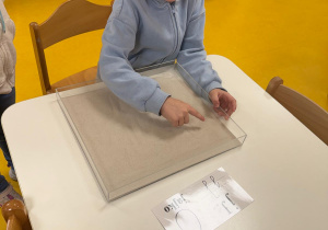 Chłopiec pisze literkę j w piasku.