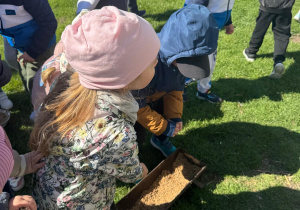 Dzieci wsypują ziarno dla kur.