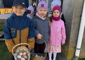 Dzieci pozują do zdjęcia z koszyczkiem z jajkami.