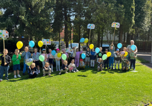 Dzieci pozują do wspólnego zdjęcia z plakatami i kolorwymi balonami w ręku.