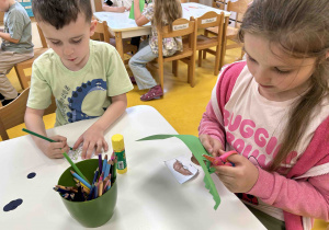 Dzieci wykonują pracę plastyczną przy stoliczku.