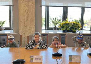 Dzieci siedzą w sali konferencyjnej.