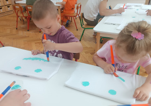 Przedszkolaki malują uśmiechy na bluzkach.