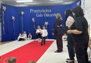 Dzieci prezentują Oscara na czerwonym dywanie.