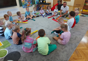 Dzieci siedzą w kole i grają na kolorowych bum bum rurkach.