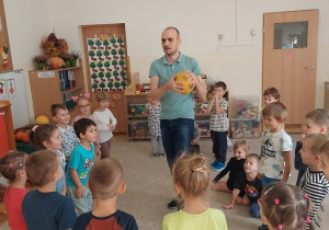 Nauczyciel rzuca piłkę do dzieci stojących w kole